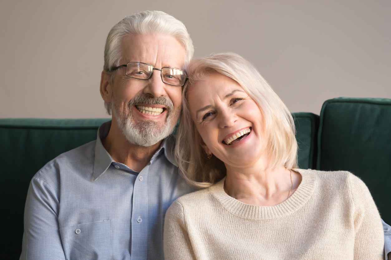 Head shot laughing retirees pretty couple sitting on couch at home, spouses having candid healthy toothy smile, dental treatment check-up services for old people, medical insurance health care concept